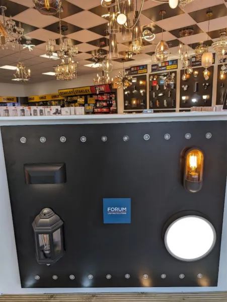 Forum display board with a black wall lantern, an amber filament wall light and a round LED bulkhead, with chandeliers behind