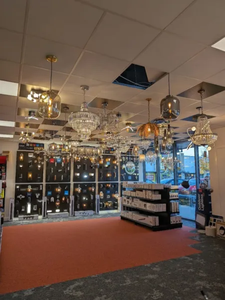 Wide view of the lighting showroom with chandeliers and pendant lights above, wall light display boards and an orange carpeted floor